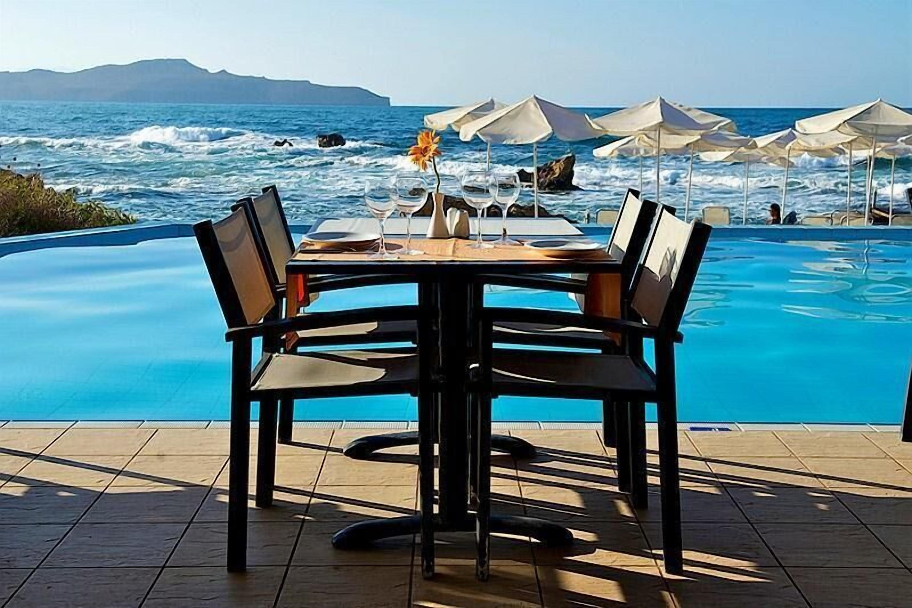 Un espace repas aménagé au bord de la piscine, avec une table dressée pour quatre personnes, offrant une vue sur l’océan.
