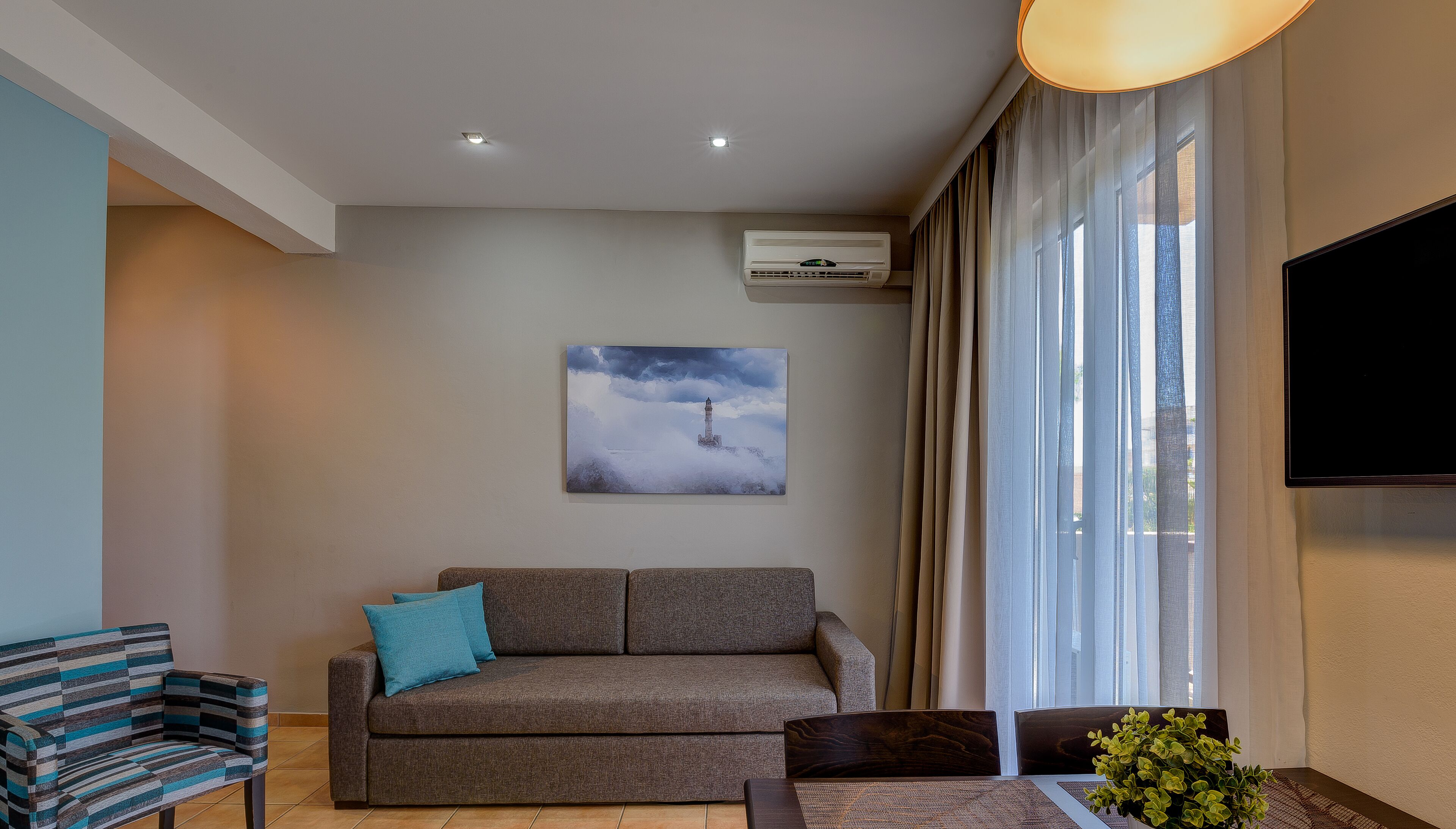 A modern living room with a sofa, a chair, a flat-screen TV, and a painting of a lighthouse.