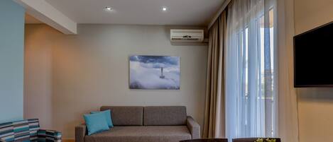 Una sala de estar moderna con un sofá, una silla, un televisor de pantalla plana y un cuadro de un faro.