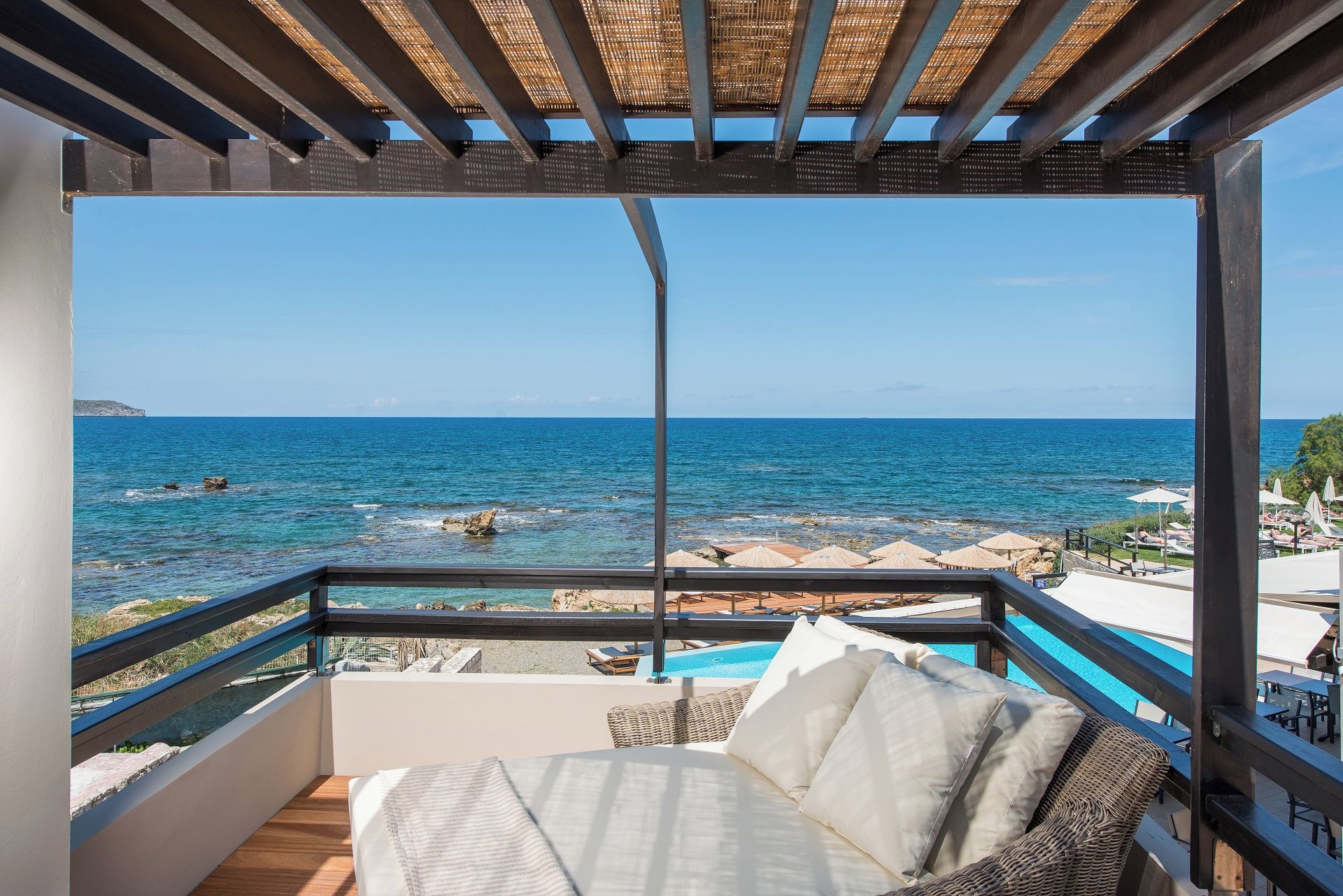 A balcony with a view of the sea, a pool, and outdoor seating.