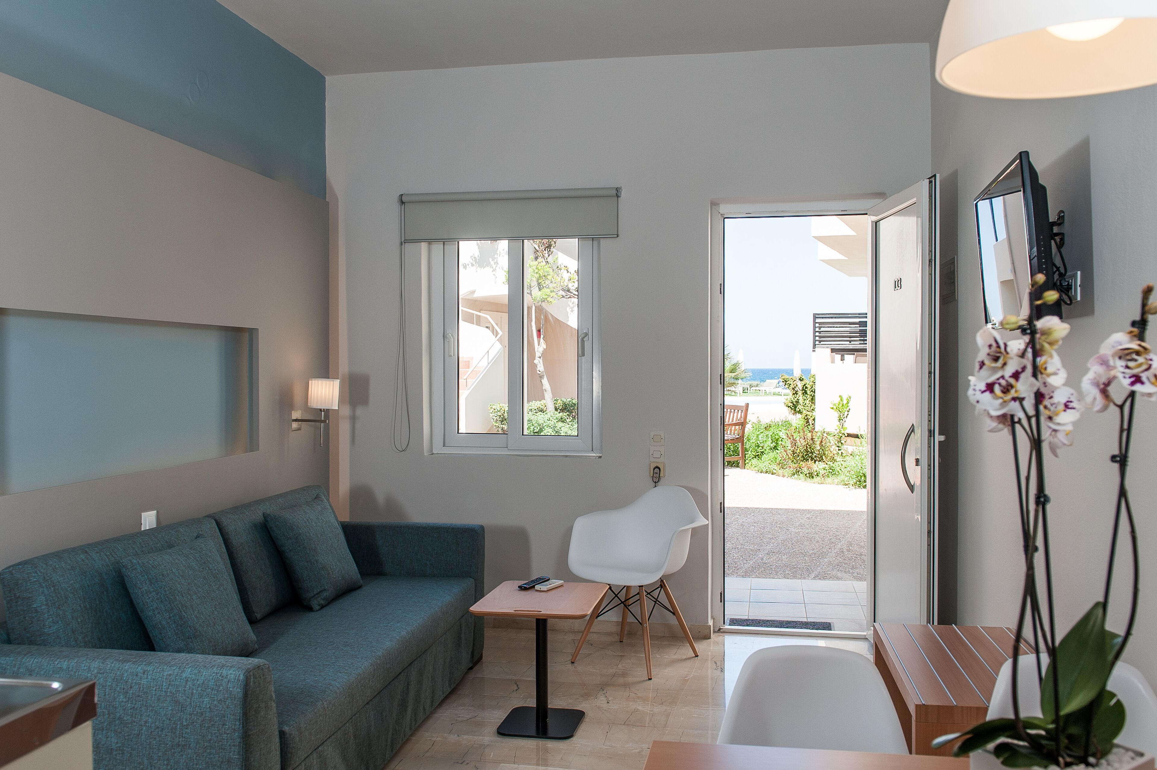 A modern room with a sofa, a small table, a chair, a bathroom, and a view of the outdoors.