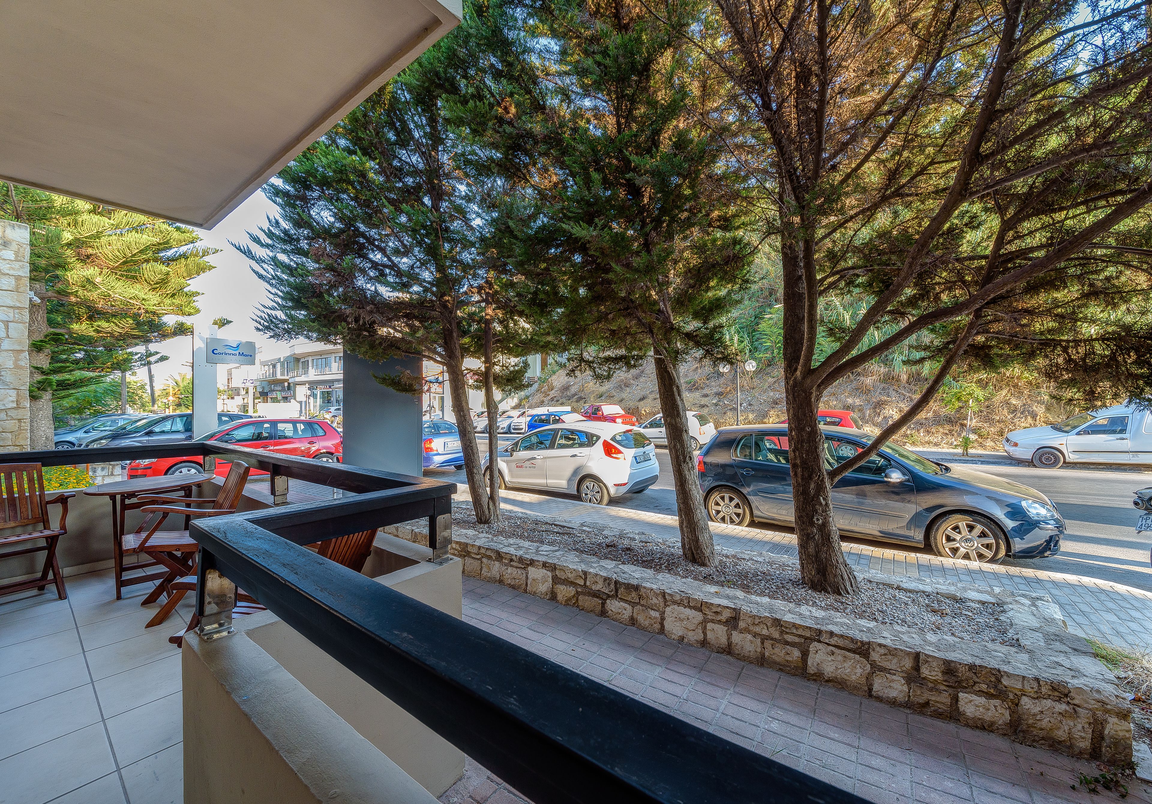 Un balcon avec des sièges, des arbres et une vue sur les voitures garées dans la rue.