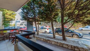 Varanda com área de estar ao ar livre, árvores e vista para carros estacionados na rua.