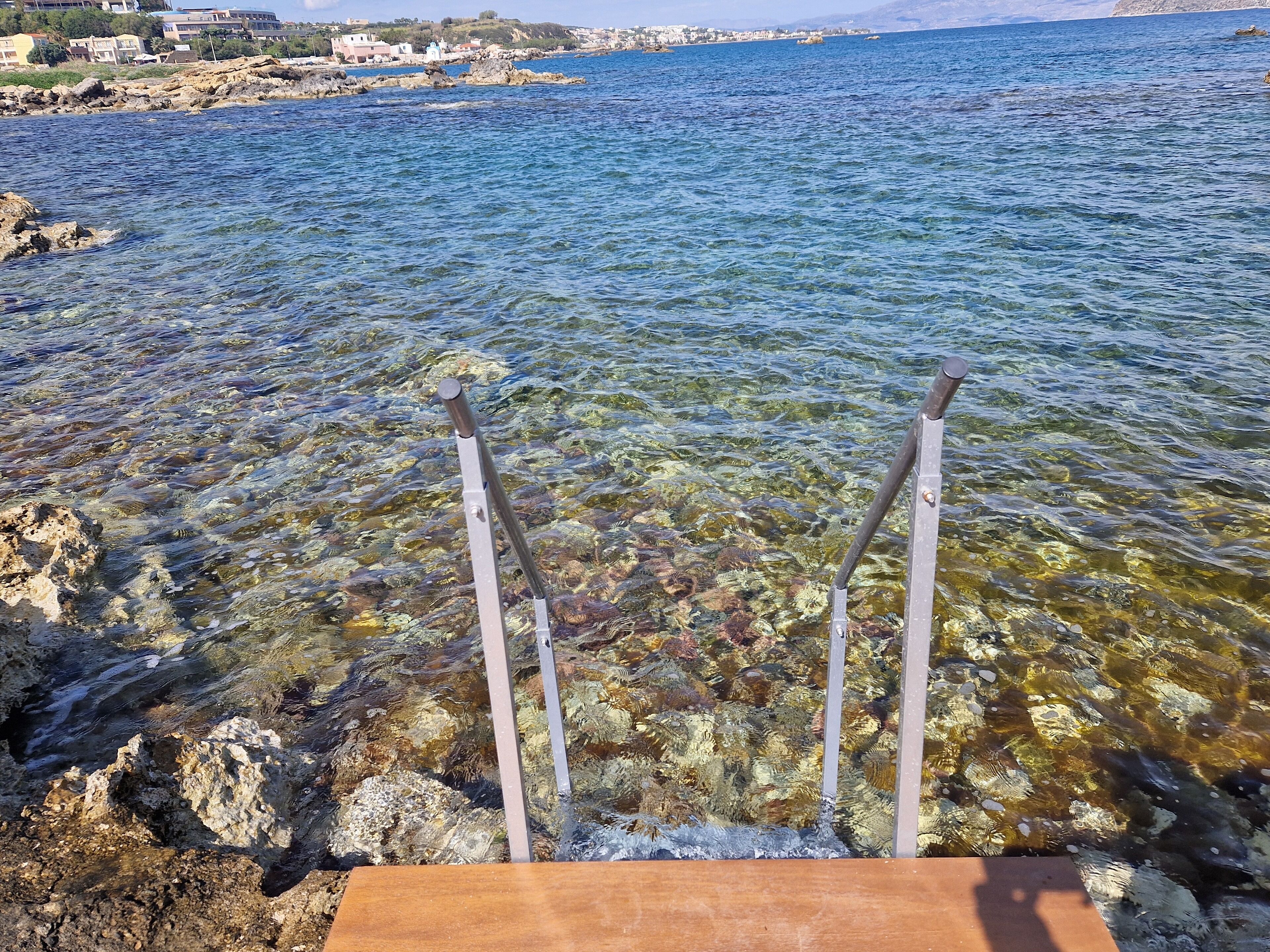 A clear view of a rocky shoreline with a wooden platform extending into the water.