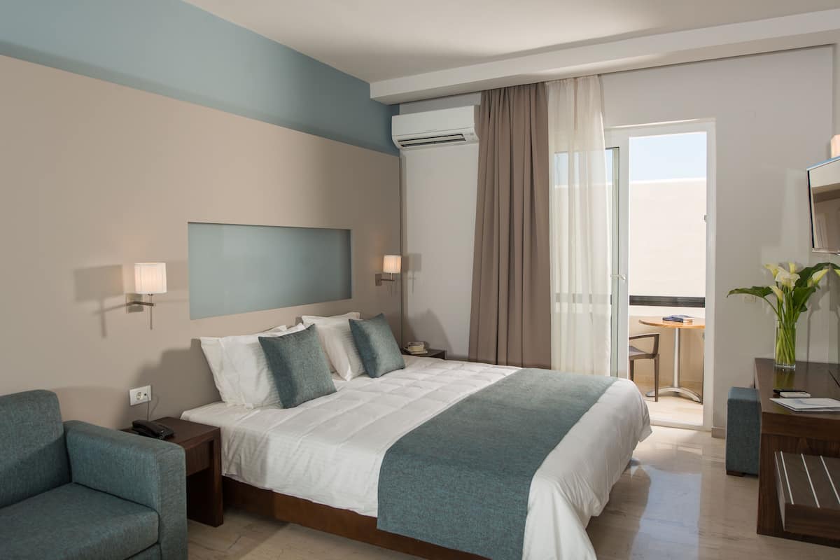 A modern hotel room with a large bed, bedside tables, a desk, and a balcony with a view.