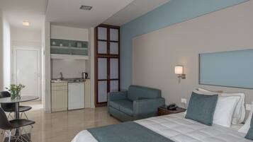 A modern hotel room with a bed, a sofa, a dining table, and a kitchenette.