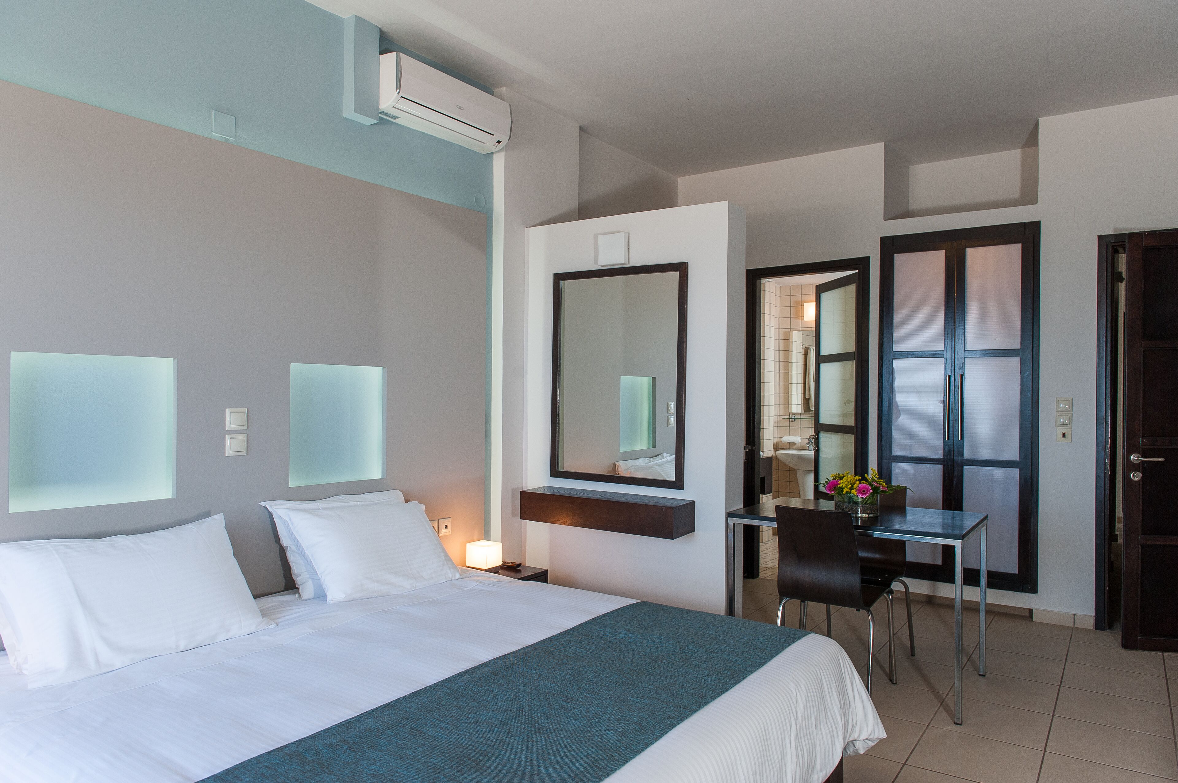 Une chambre d’hôtel avec un grand lit, un bureau, une chaise, un miroir et un appareil de climatisation.