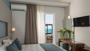 A hotel room with a bed, a desk, a TV, and a view of the sea through an open door. - Corinna Mare (Chania)