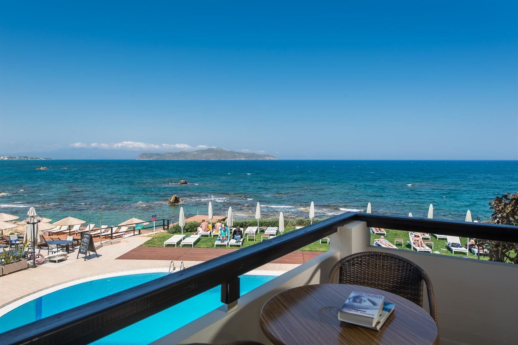 Een balkon met uitzicht op zee, lounge fauteuils en een zwembad.