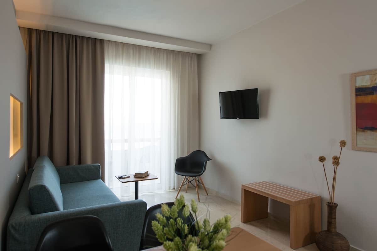 A modern living room with a sofa, a chair, a small table, a TV mounted on the wall, and a vase with dried flowers.