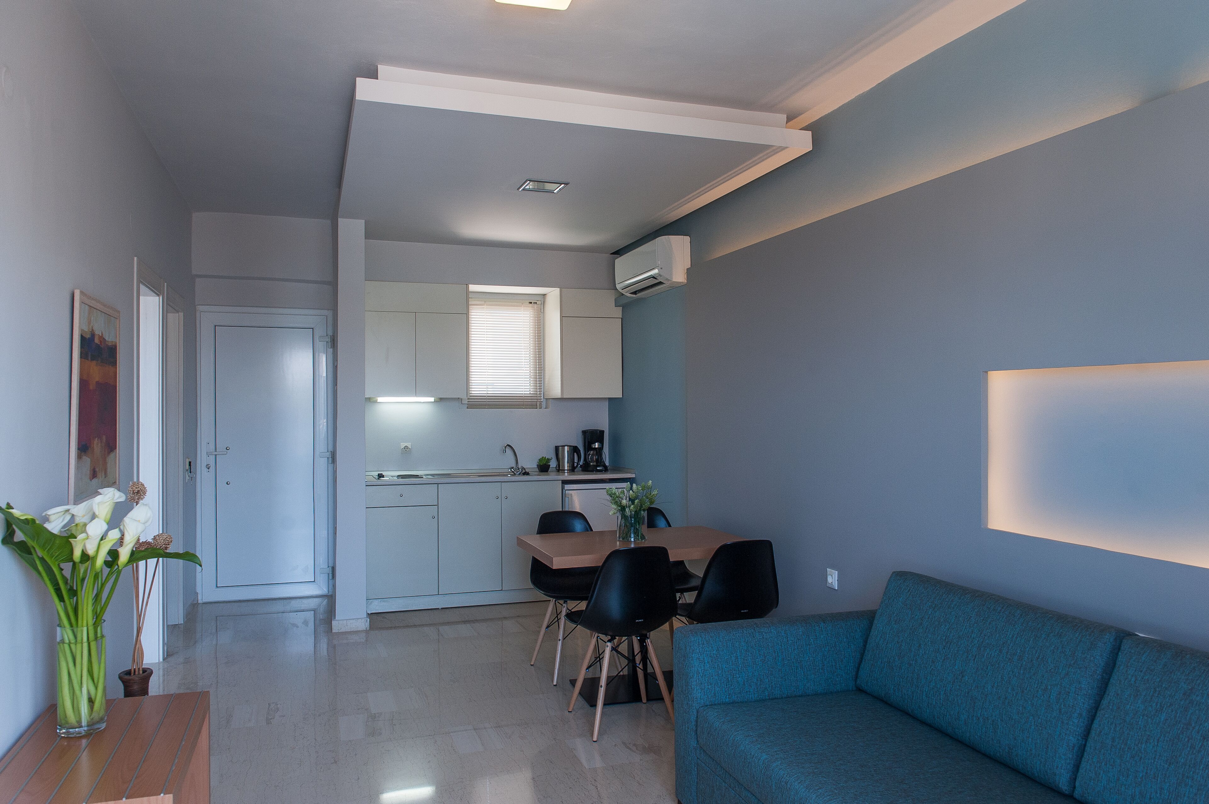 Un salon moderne avec un canapé bleu, une table à manger avec des chaises et un coin cuisine avec une fenêtre.