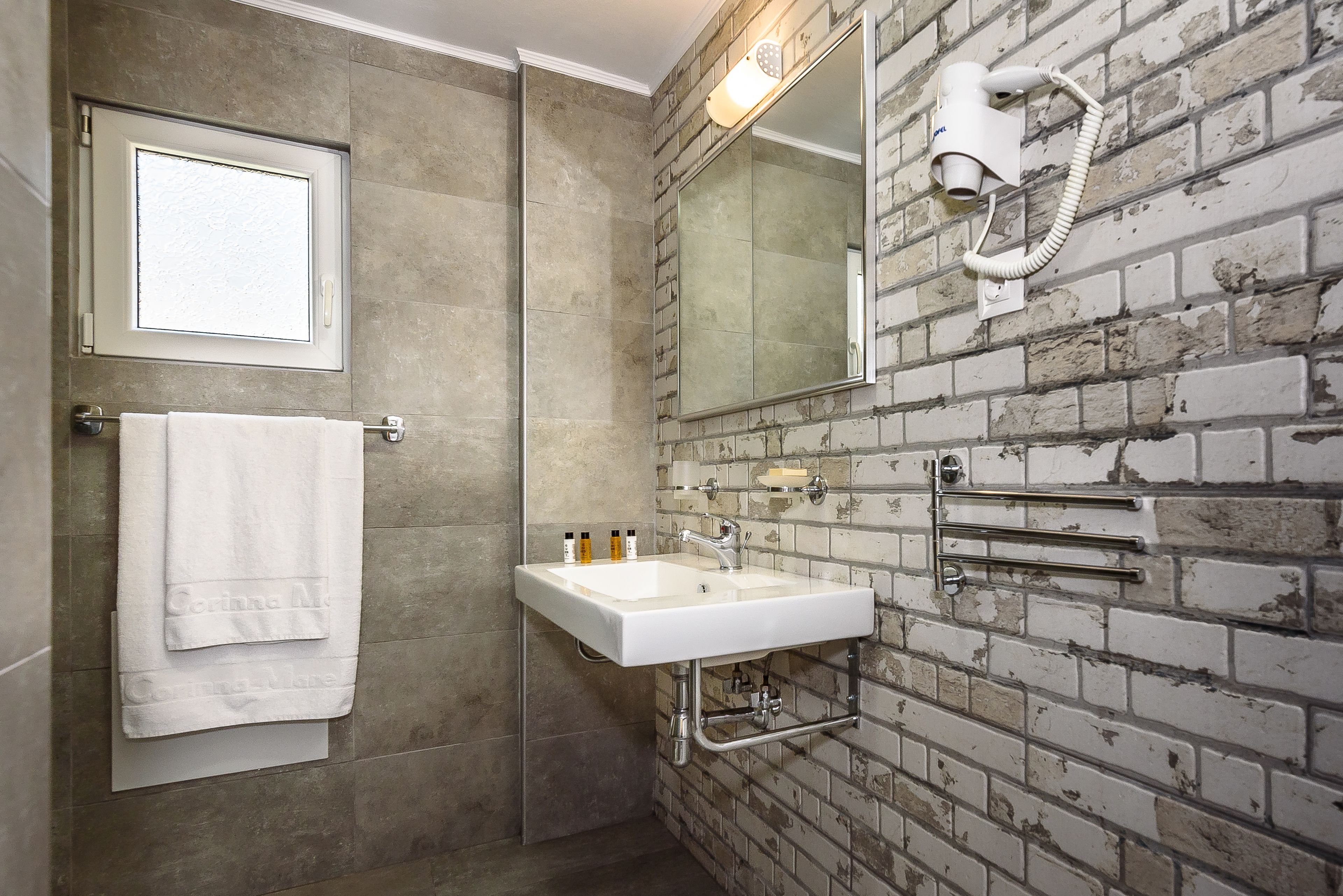 Une salle de bain avec un lavabo blanc, un porte-serviettes avec une serviette blanche, un miroir et un sèche-cheveux fixé au mur.