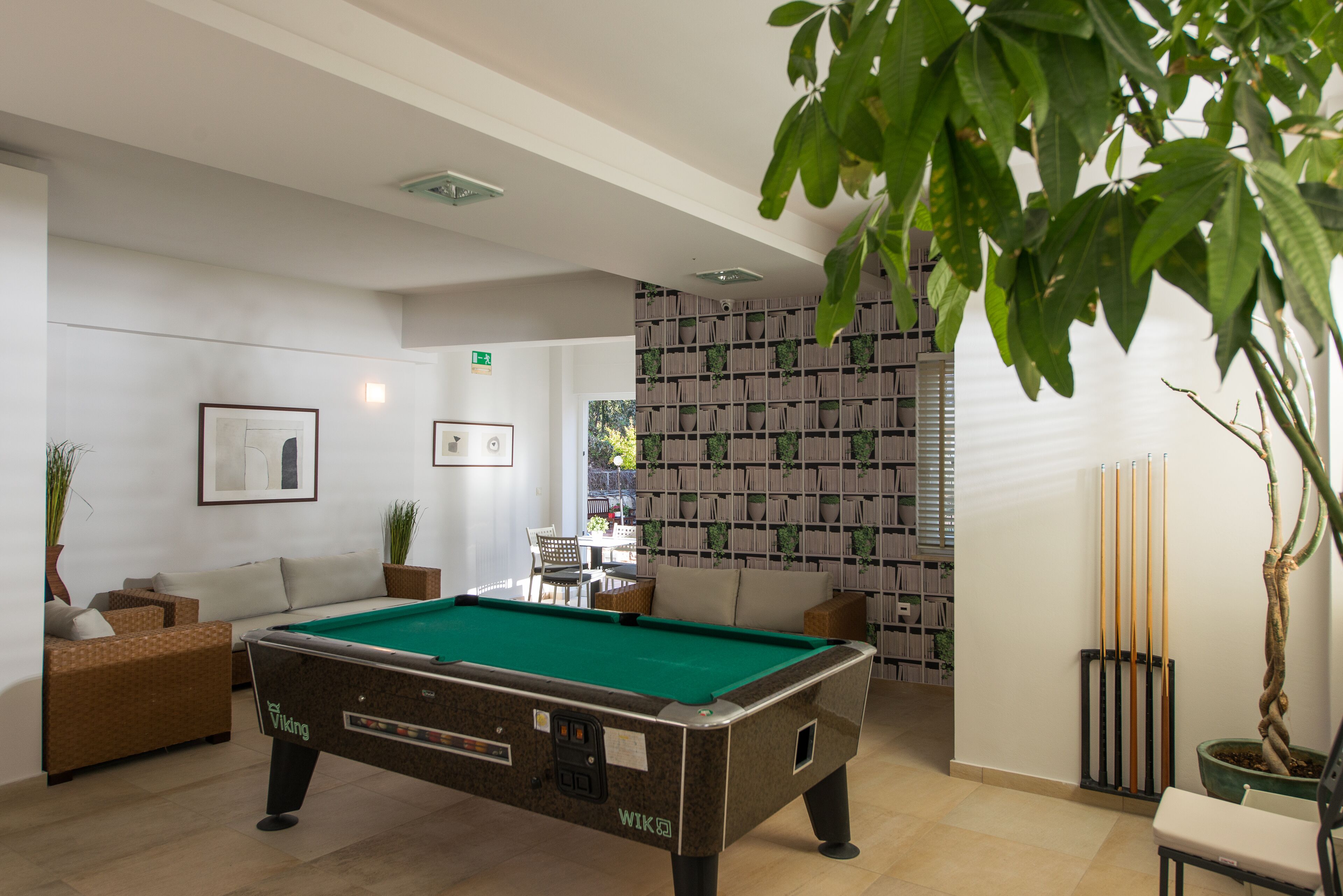 A pool table in a room with a sofa, a small table with chairs, and a wall with a patterned design.