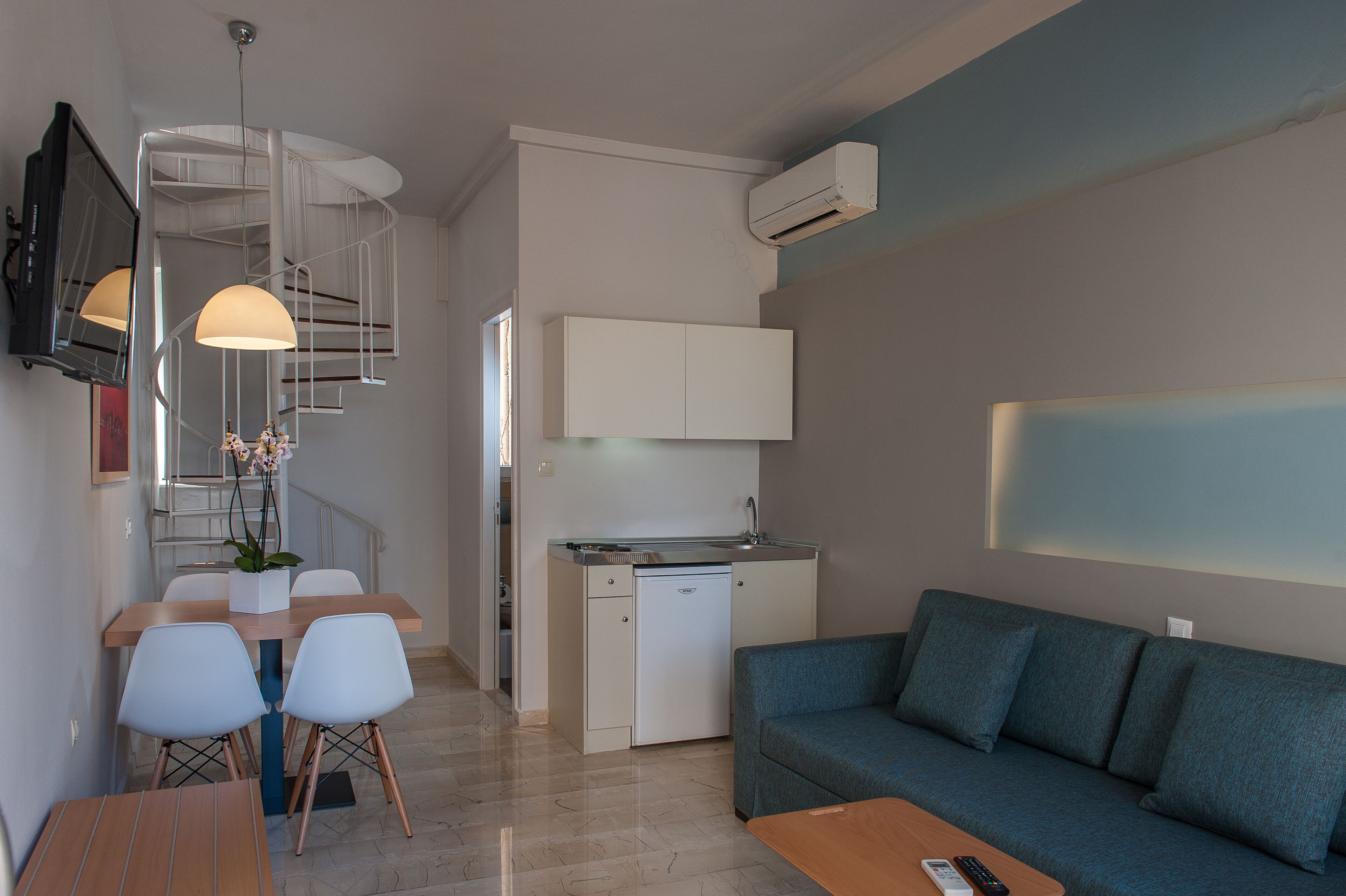 A compact living space with a kitchenette, a dining area with chairs, a sofa, and a TV mounted on the wall.