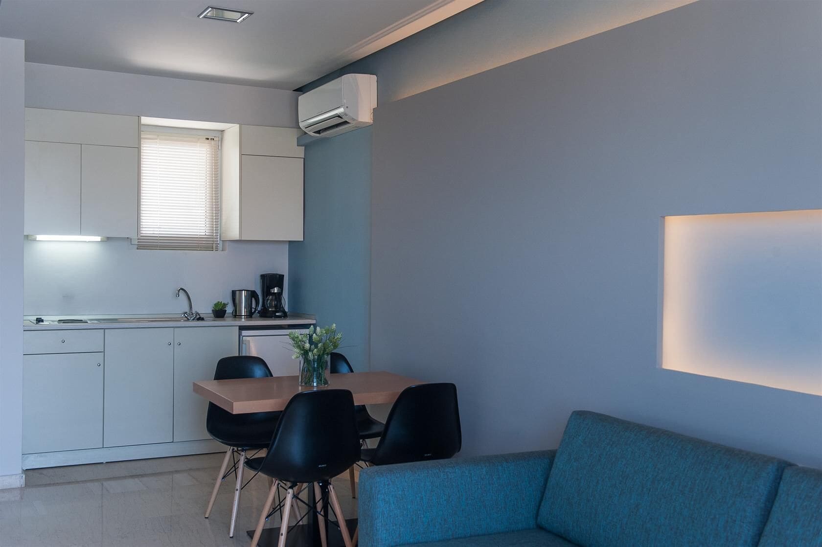 A modern kitchen with white cabinets, a coffee maker, and a dining area with a table and chairs.