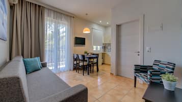Una sala de estar con un sofá, una mesa de comedor con sillas, un televisor montado en la pared y una puerta que da a la cocina.
