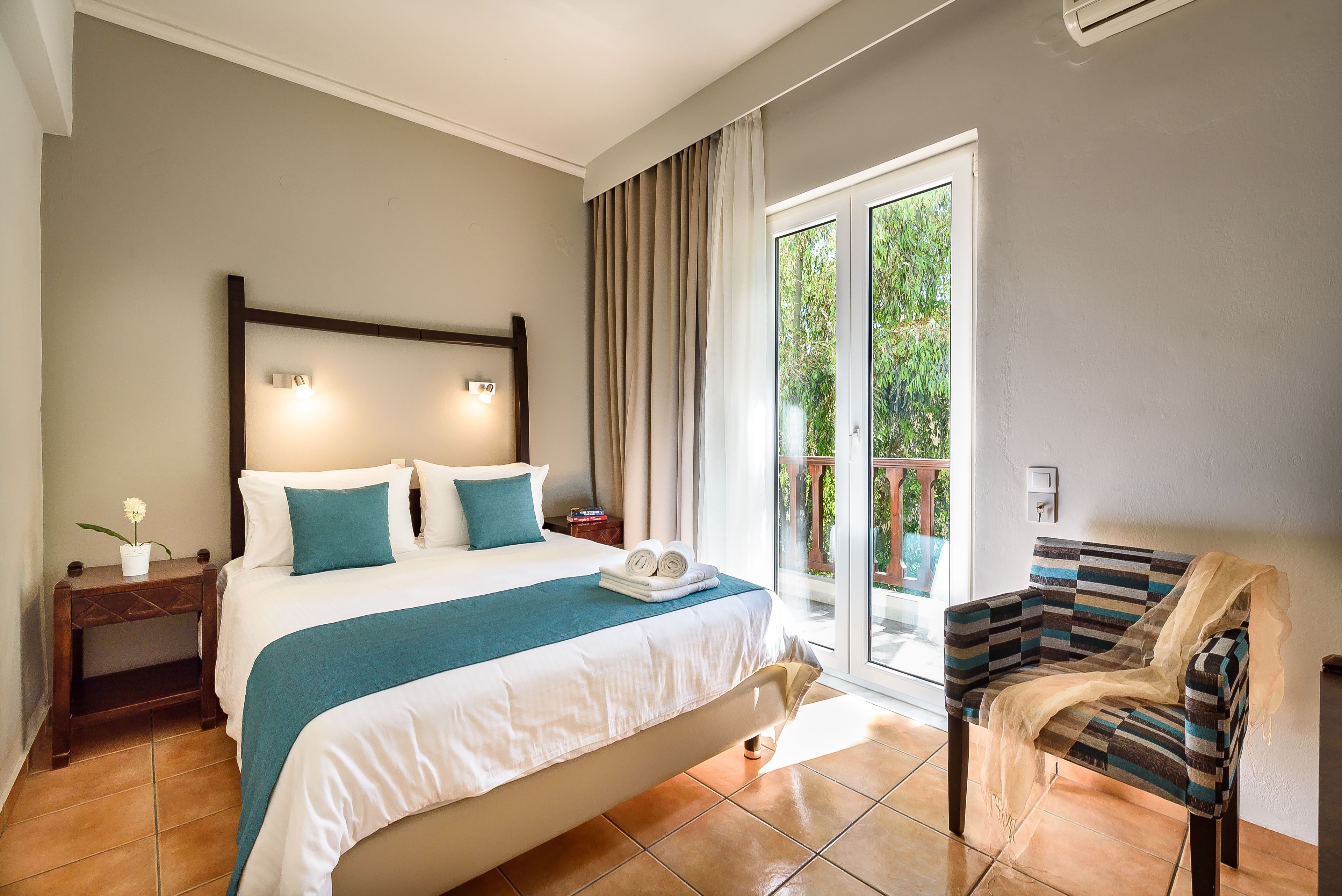 Ein Hotelzimmer mit Bett, Nachttisch, Stuhl und Blick ins Freie.
