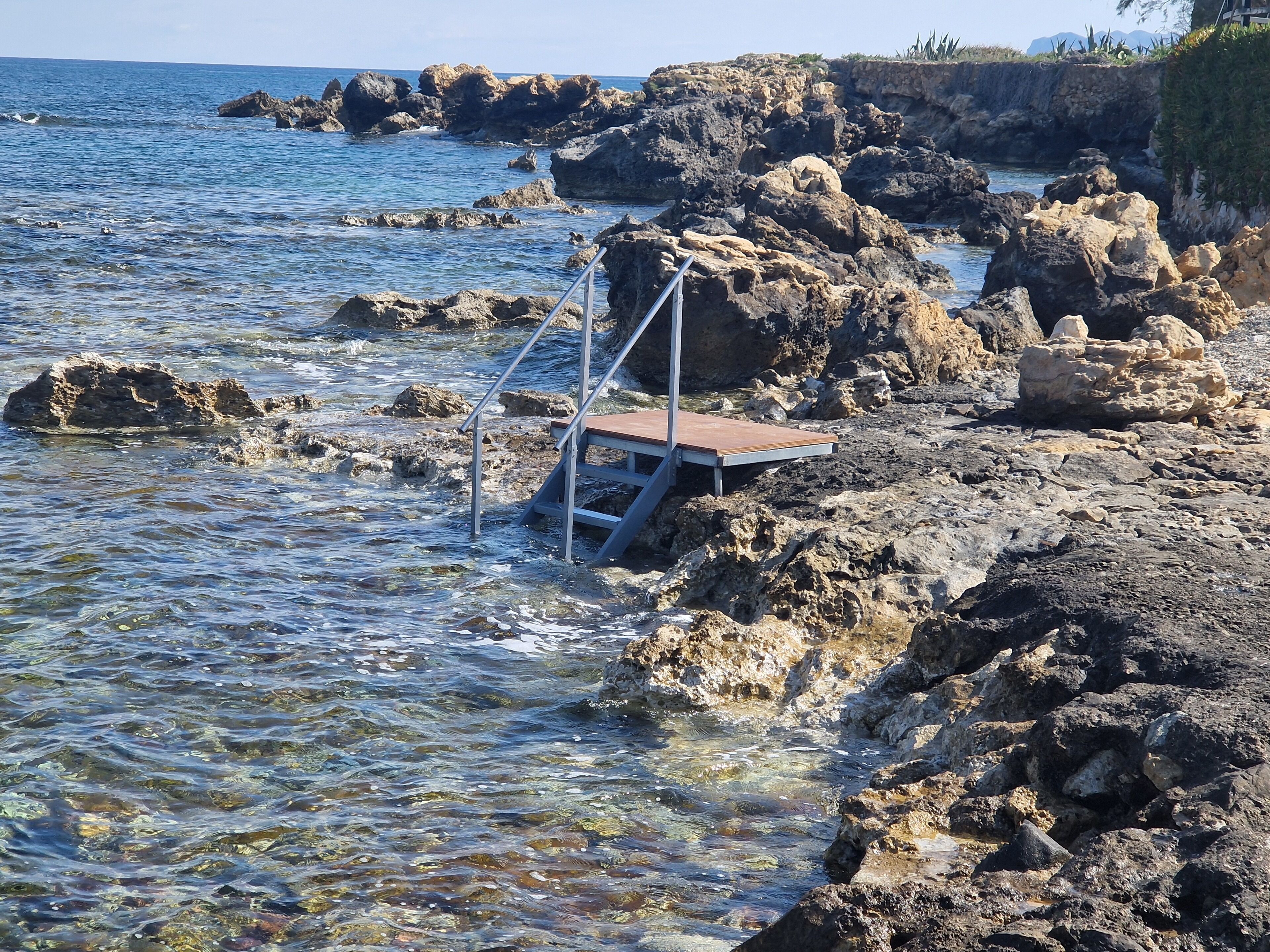 Eine felsige Küste mit einer Metalltreppe, die ins Wasser führt.