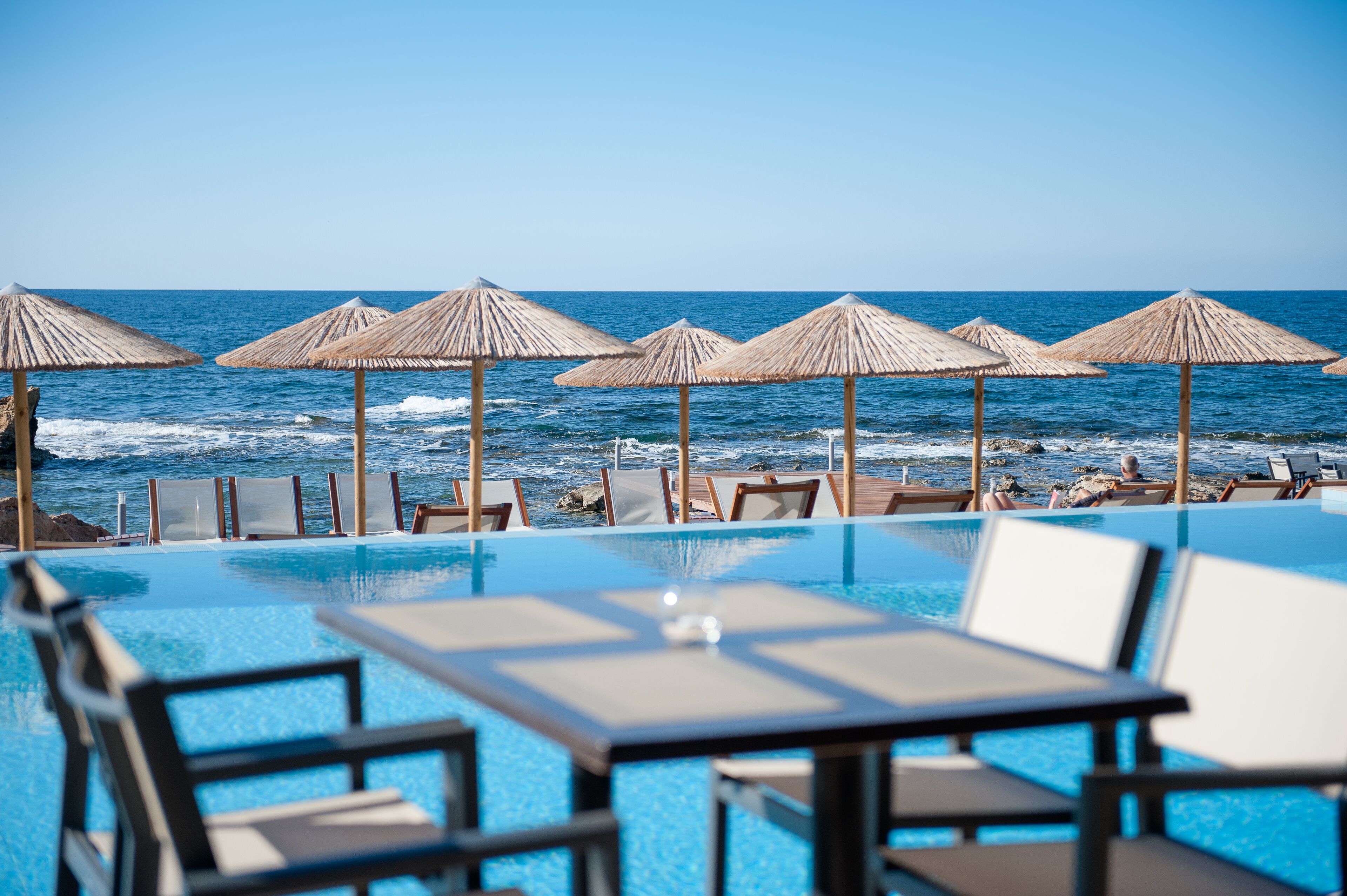 Una piscina infinita con asientos y sombrillas a la orilla de la playa, con vista al océano.