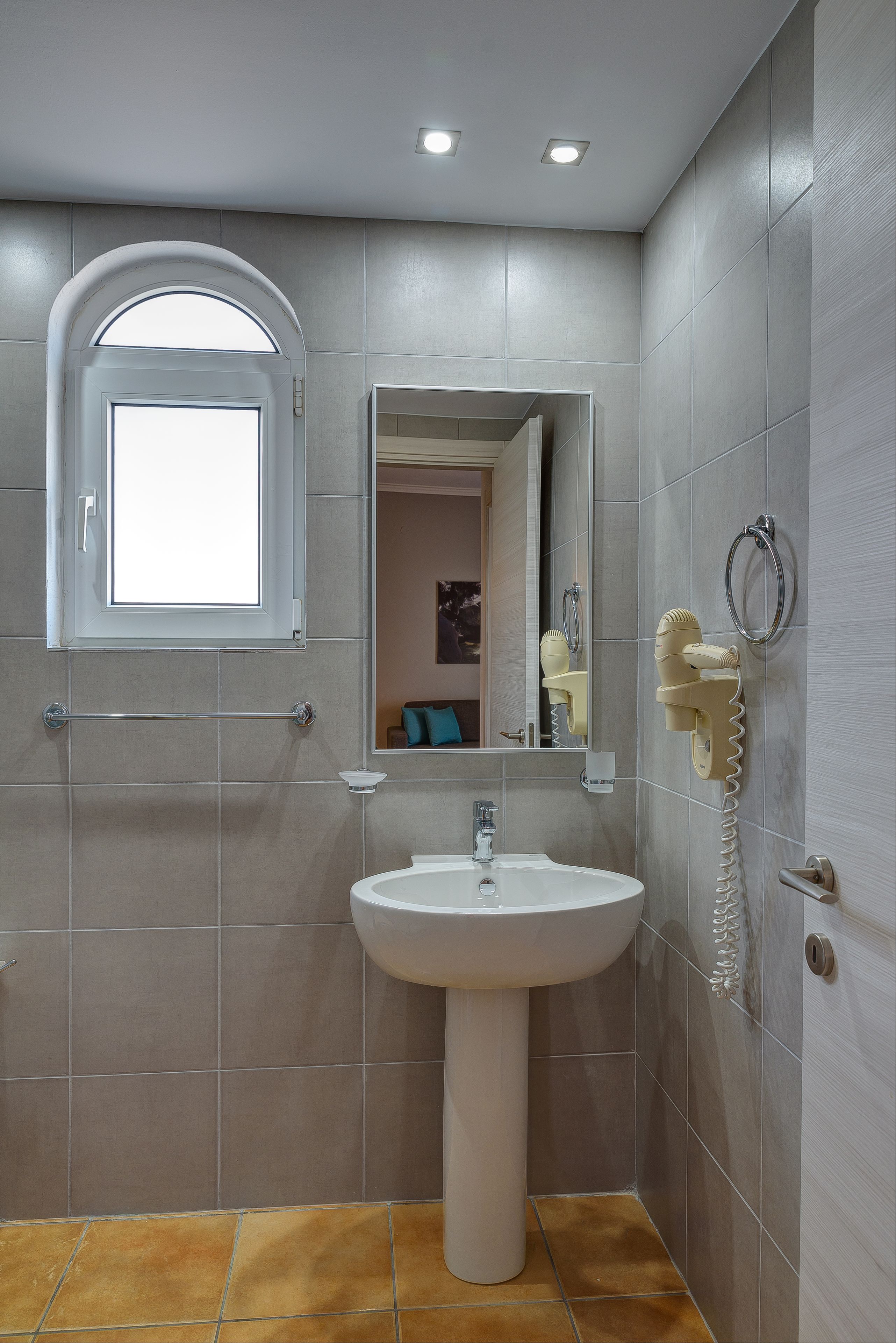 Ein Badezimmer mit einem Standwaschbecken, einem Spiegel, einem Handtuchhalter und einem Fenster.
