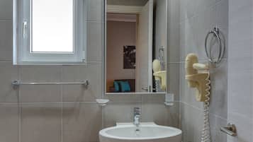 Un baño con lavamanos pedestal, un espejo, toallero y una ventana.