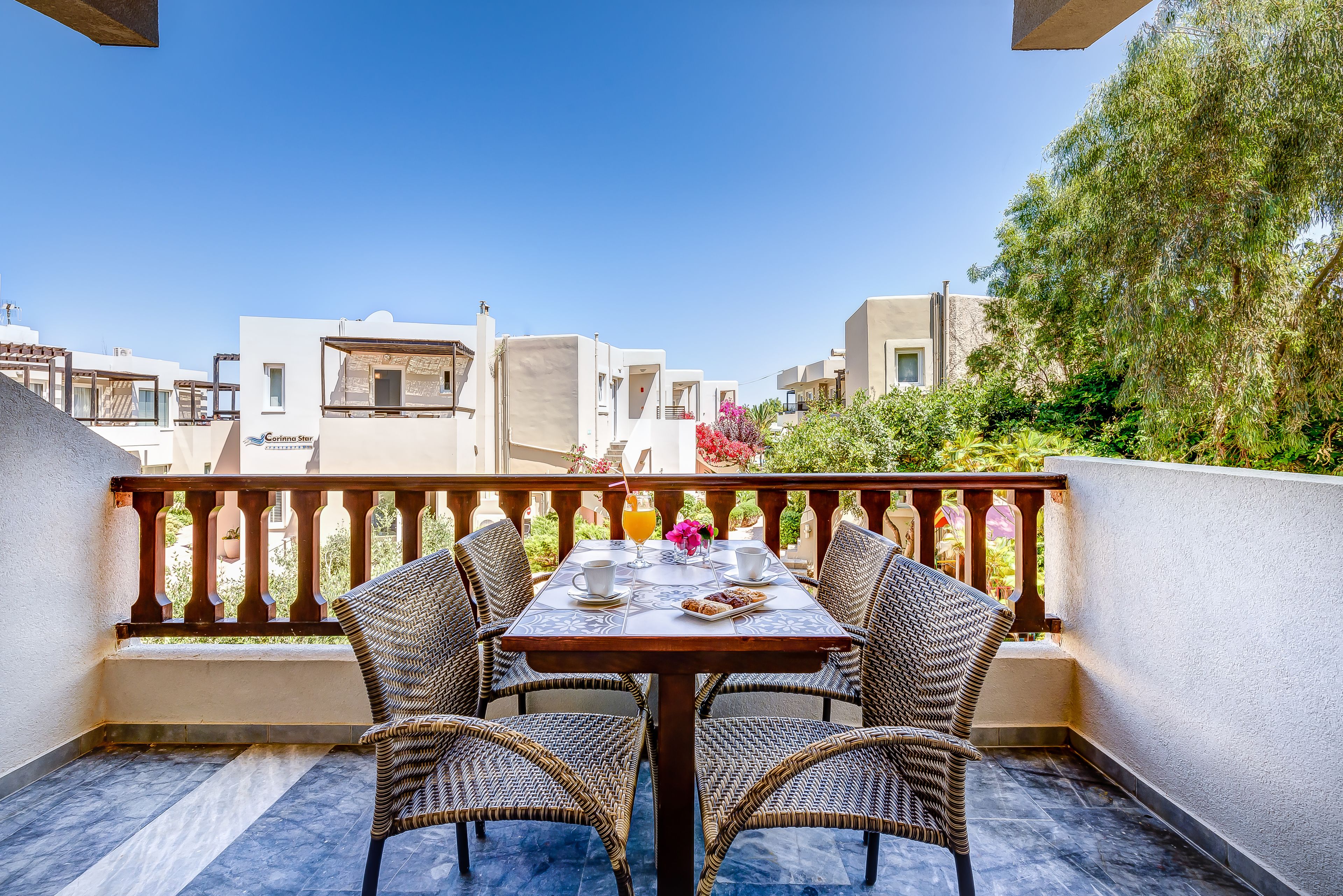 Ein Balkon mit Tisch für Zwei, Korbstühle und Blick auf Gebäude und Grünflächen.