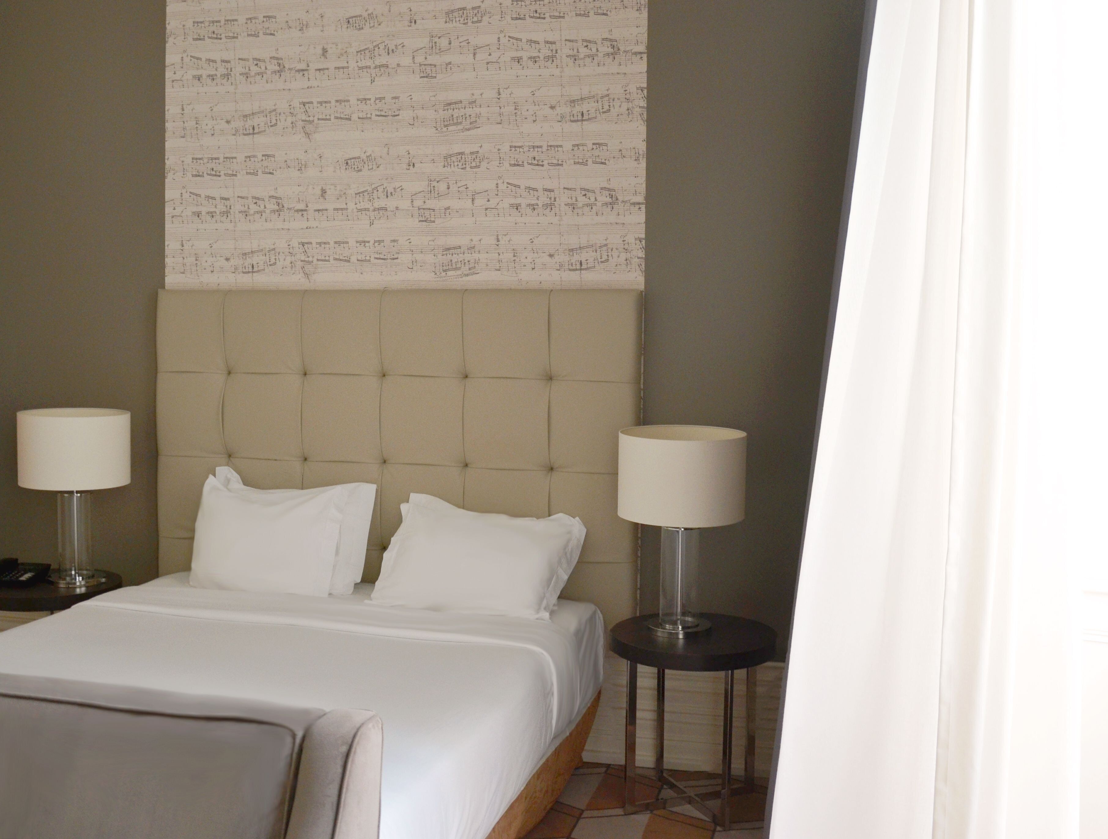 Ein Hotelzimmer mit einem großen Bett, zwei Nachttischen mit Lampen, einem Kopfteil mit Notenmuster und einem gefliesten Boden.