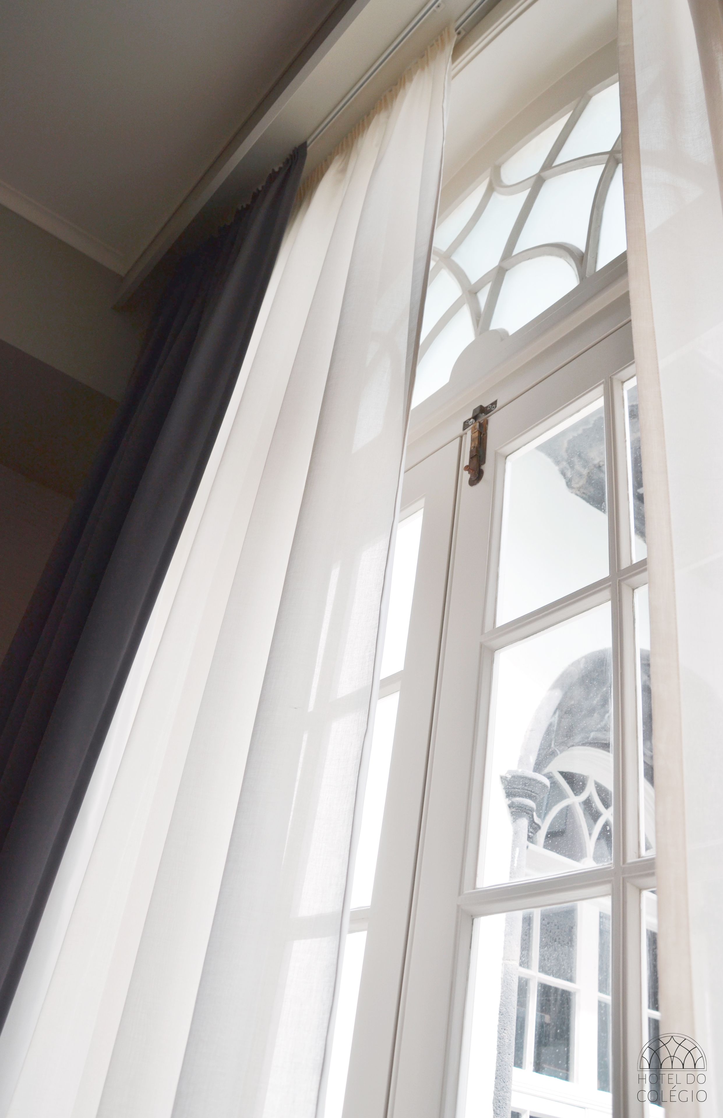 Una ventana con cortinas blancas, vista de un edificio con fachada blanca y un marco de ventana decorativo.