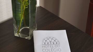 Un jarrón de cristal transparente con flores amarillas y un folleto sobre una mesa de madera.