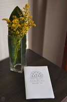 Un jarrón de cristal transparente con flores amarillas y un folleto sobre una mesa de madera.