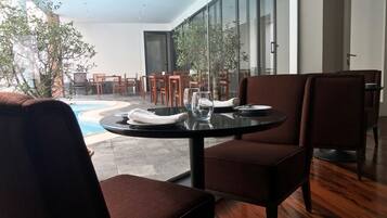 Un coin repas avec une table ronde, des chaises à revêtement marron et une vue sur une piscine extérieure et des chaises de patio.