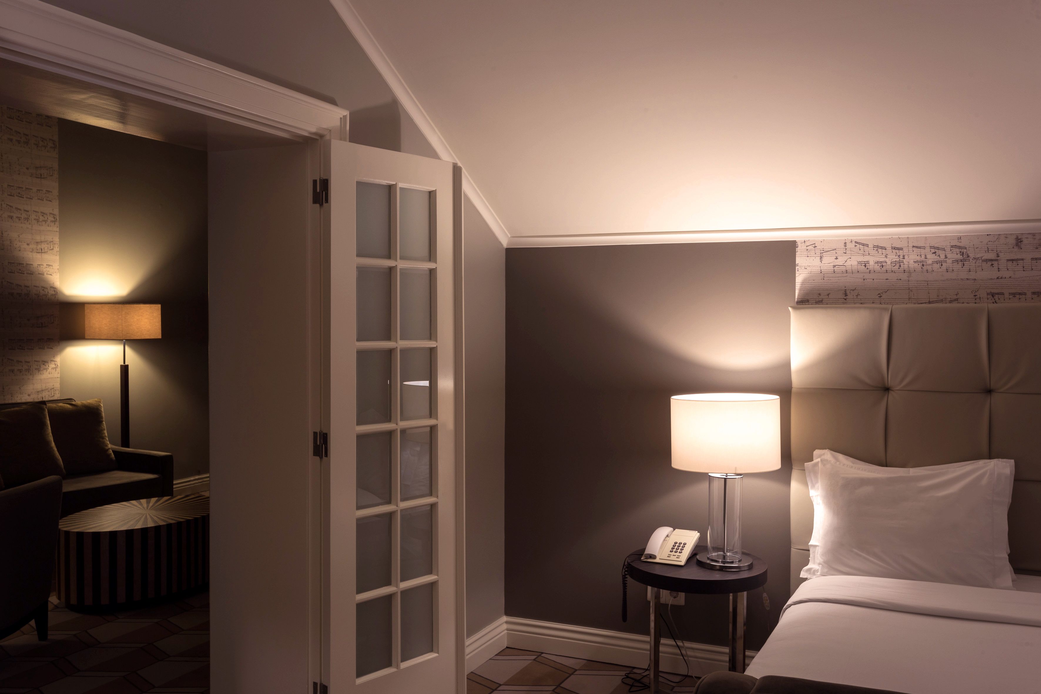 A hotel room with a bed, a nightstand with a lamp, a chair, and a small table with a telephone.