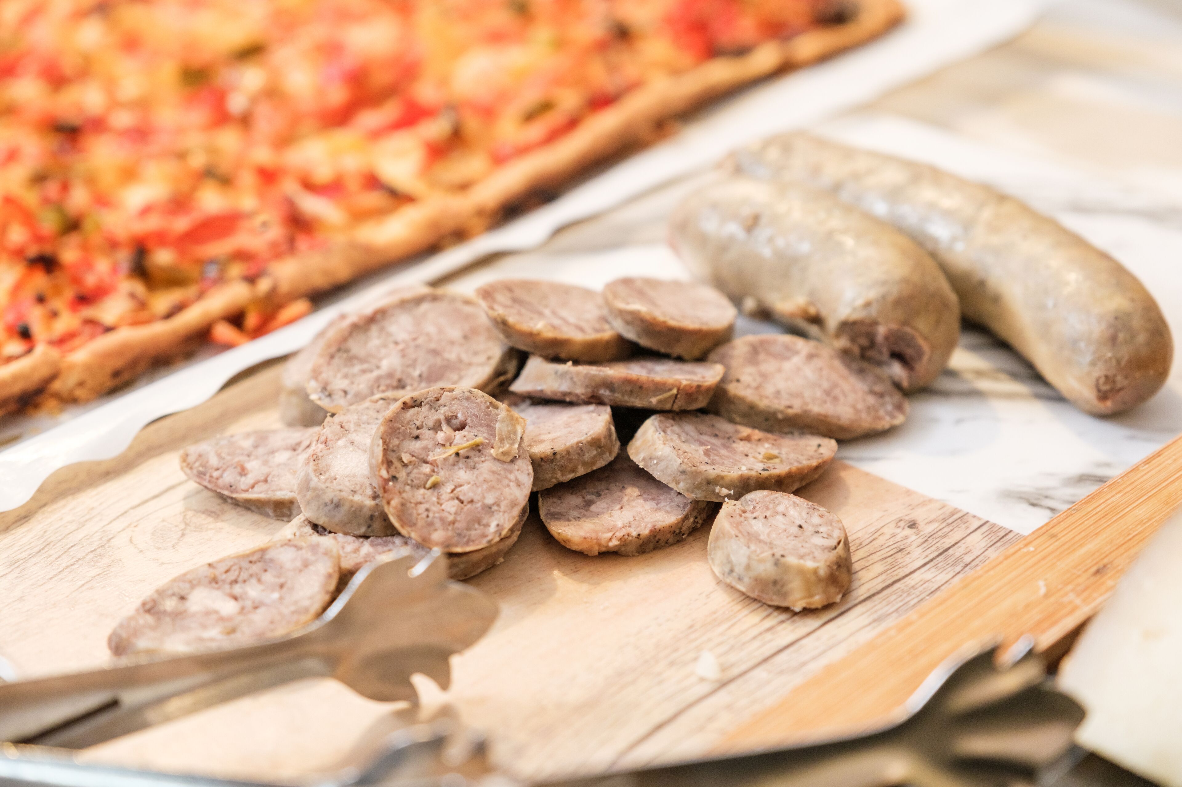 Sliced sausages and a pizza on a wooden board.