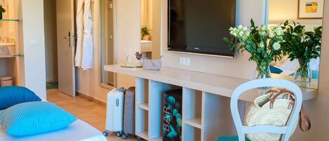 Habitación de hotel con cama, escritorio con televisor, silla, maleta y un florero con flores.