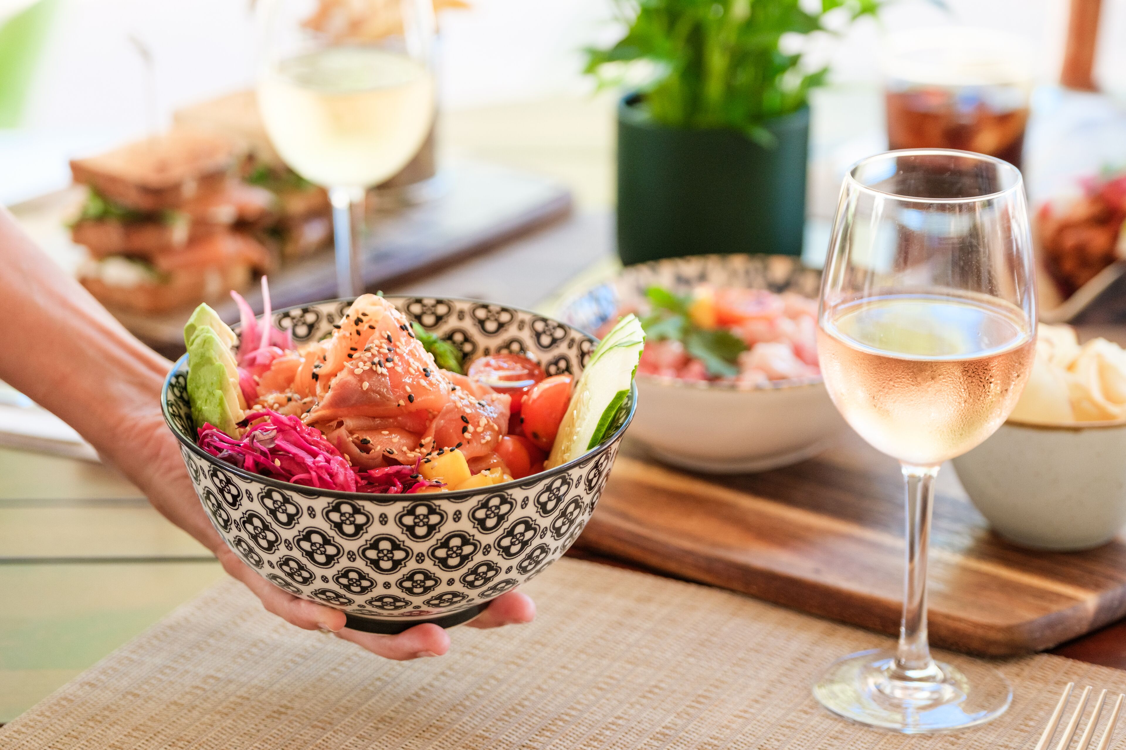 A person holding a bowl of sushi with a glass of white wine nearby.