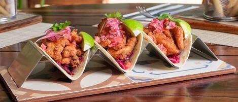 Three tacos on a wooden table with a metal tray.
