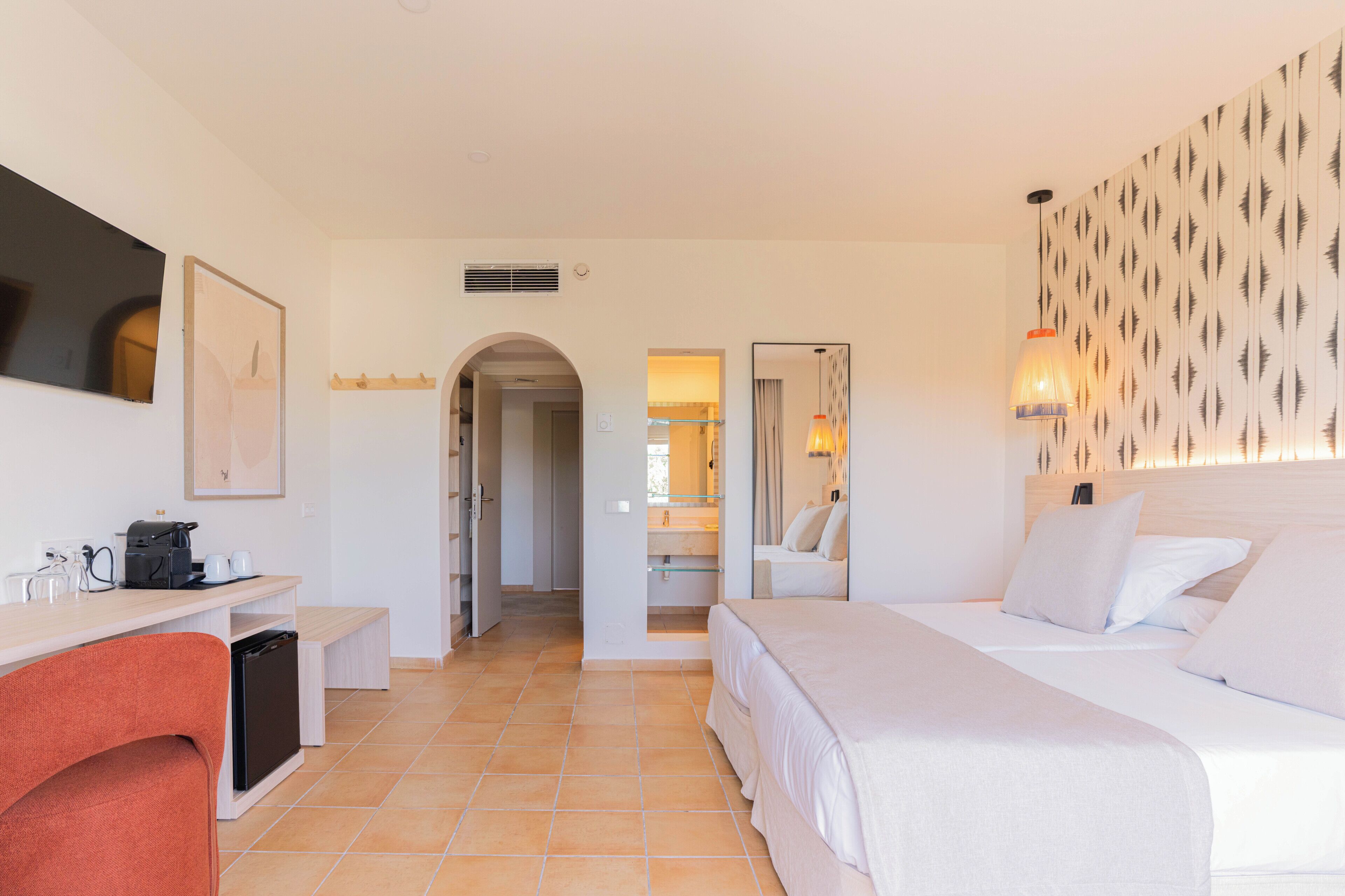 Habitación de hotel con cama, escritorio con cafetera, una silla y televisor.