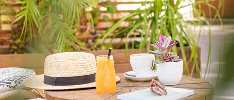 A round wooden table with a straw hat, a glass of orange juice, a white cup, a small potted plant, and a notebook.
