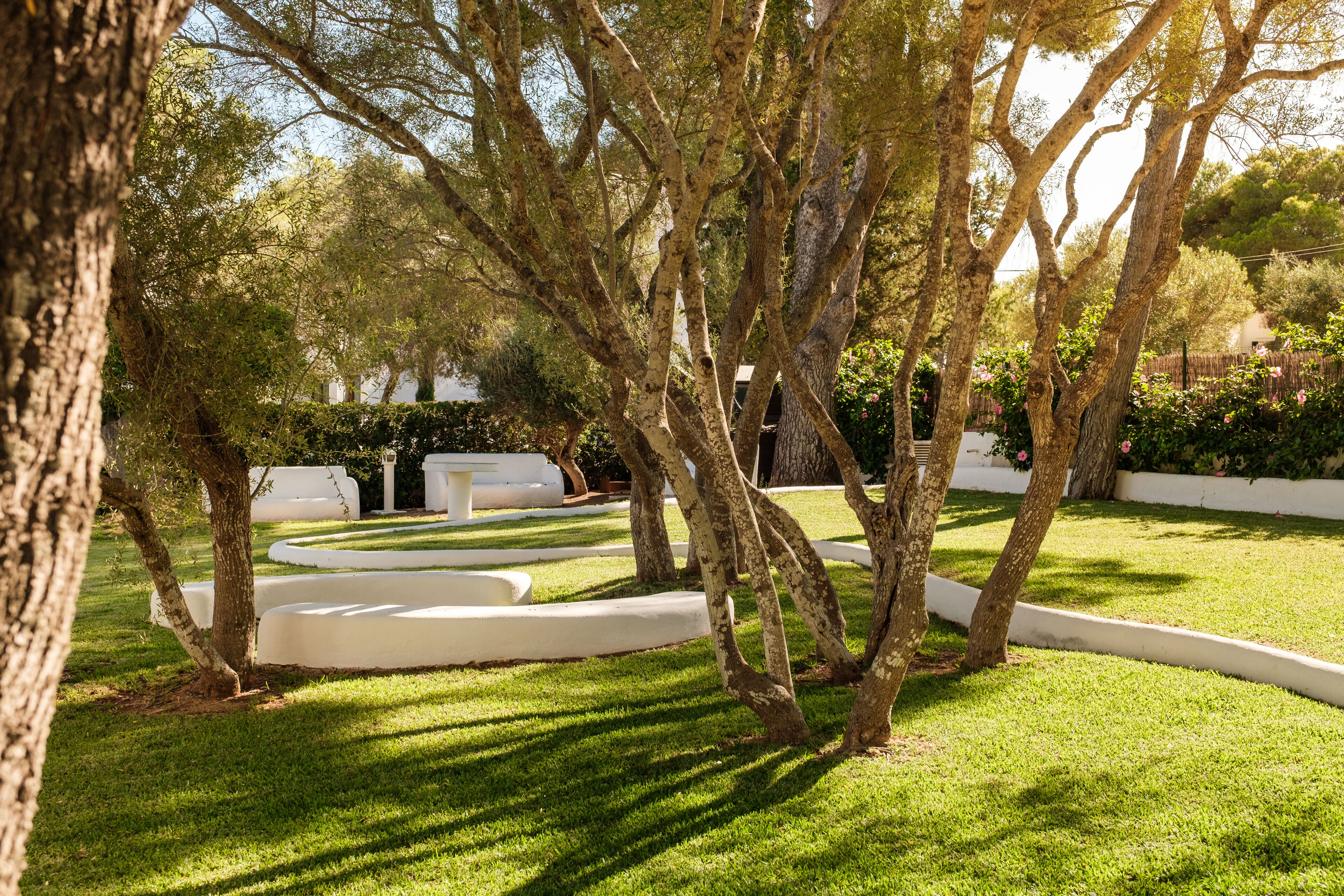 A well-maintained garden with mature trees, a neatly trimmed lawn, and a white outdoor seating area.