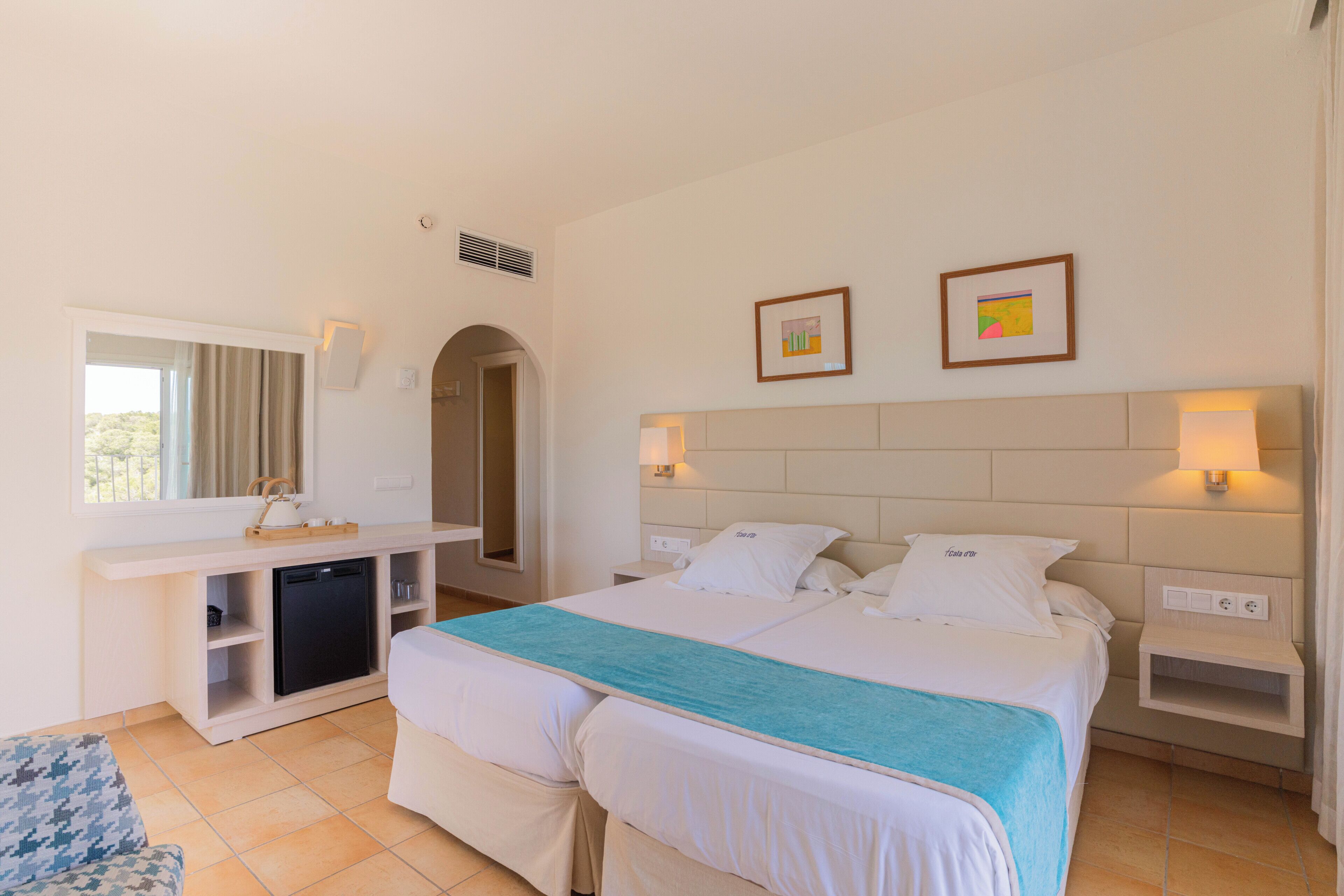 A hotel room with a bed, bedside tables, a desk, a chair, and a small kitchenette.