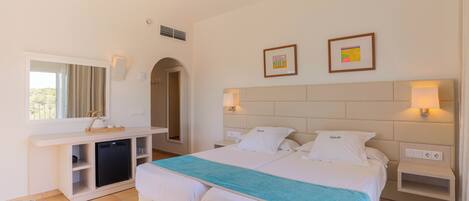 A hotel room with a bed, bedside tables, a desk, a chair, and a small kitchenette.