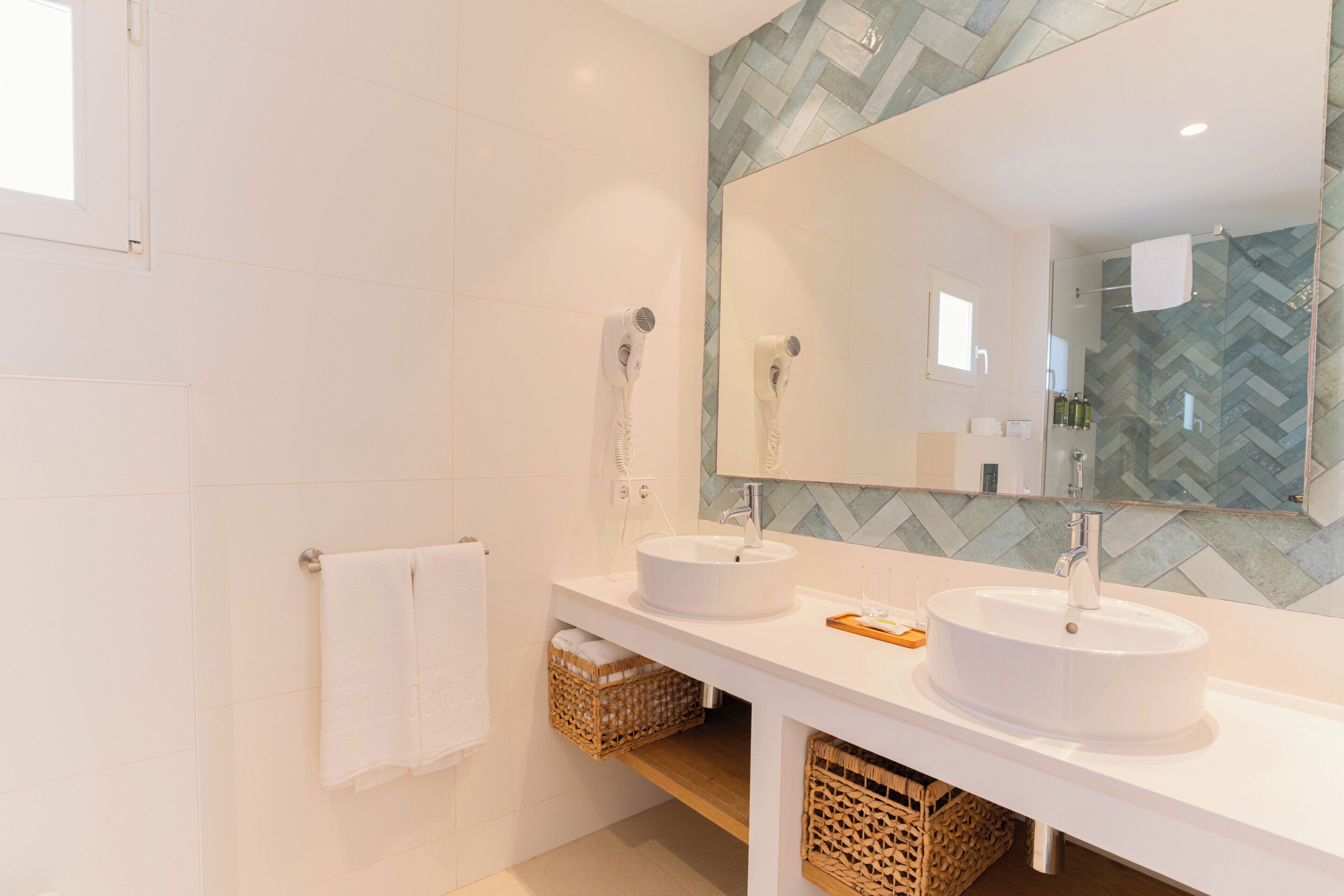 Un baño moderno con dos lavamanos, un espejo grande y un salpicadero de azulejos tipo espiga.