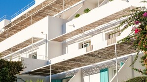 Un immeuble à plusieurs étages, aux murs extérieurs blancs, doté de balcons ornés de plantes et surmonté d’un toit de chaume.