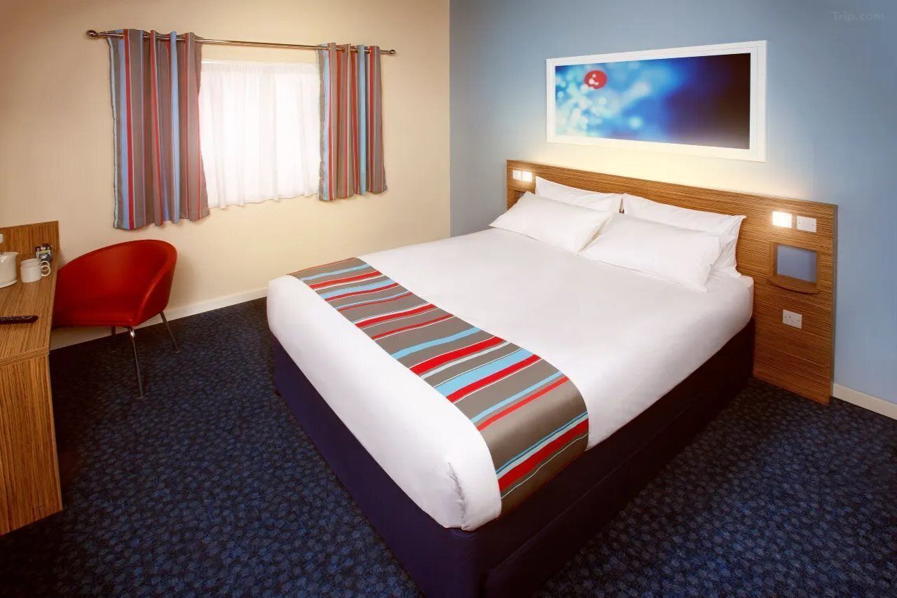 Ein Hotelzimmer mit einem großen Bett, einem roten Sessel, einem Schreibtisch mit Kaffeemaschine und einem Bild an der Wand.