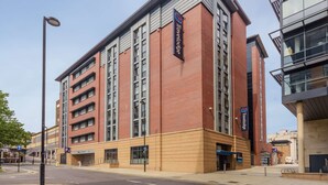 Um edifício moderno com um grande letreiro da Travelodge, com vários andares e janelas amplas.