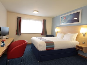 A hotel room with a bed, a desk with a computer, a chair, a TV, and a window with curtains.
