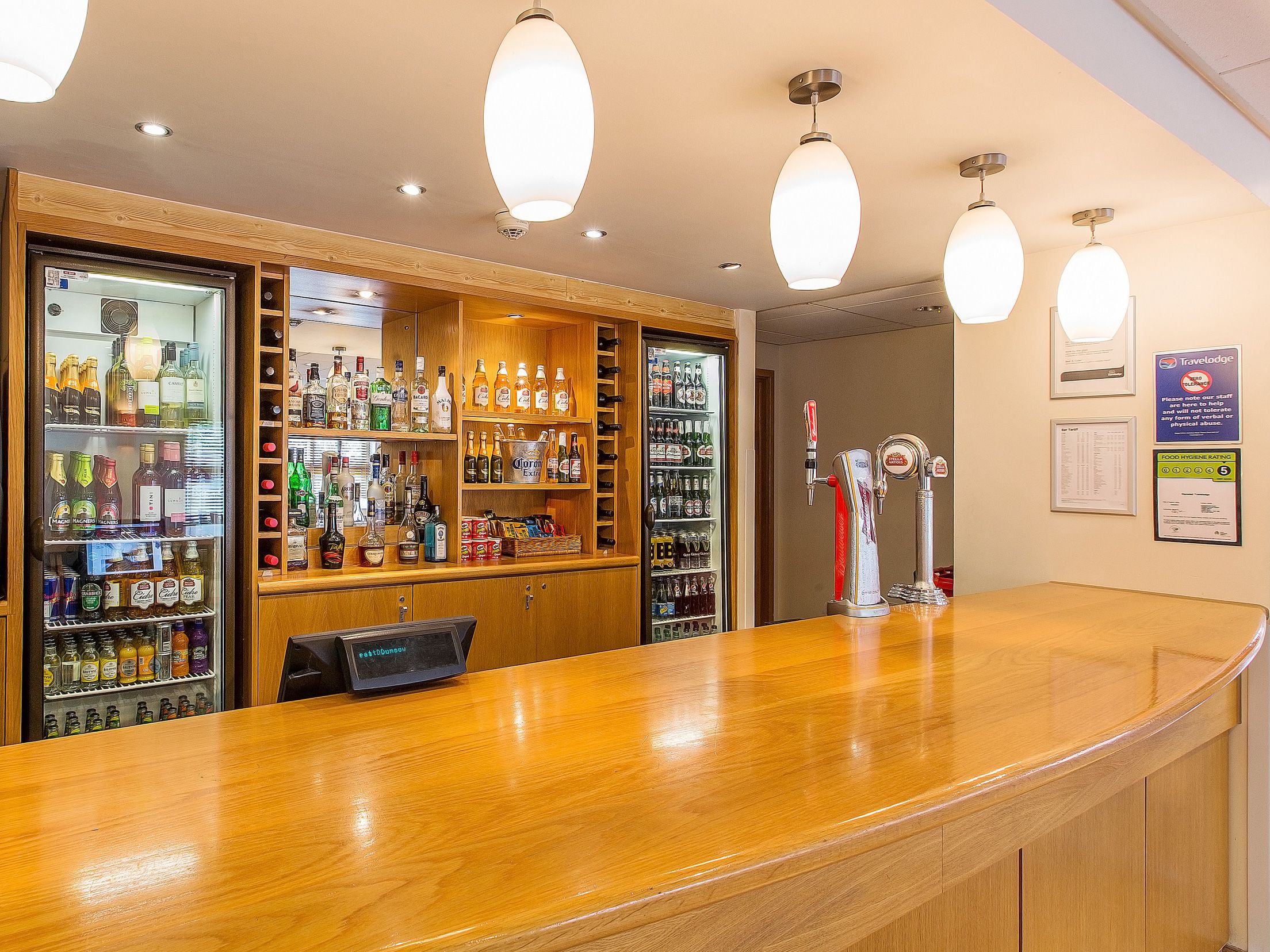 A bar area with shelves of various liquor bottles, a beer tap, and a digital display.