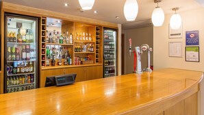 A bar area with shelves of various liquor bottles, a beer tap, and a digital display. - Travelodge Stansted Great Dunmow (Dunmow)