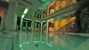 A large indoor swimming pool with a stone wall and a staircase leading to an upper level. - Hotel Sanotel (Bad Gastein)