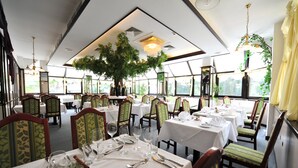 A restaurant with multiple tables set for dining, chairs with patterned upholstery, and a large tree centerpiece. - Hotel Sanotel (Bad Gastein)